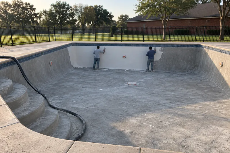 Long wall of an empty community pool getting new white plaster
