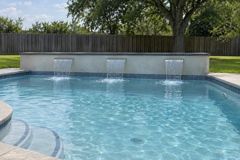 Gray stucco feature wall with sheer sheets of water falling into a pool